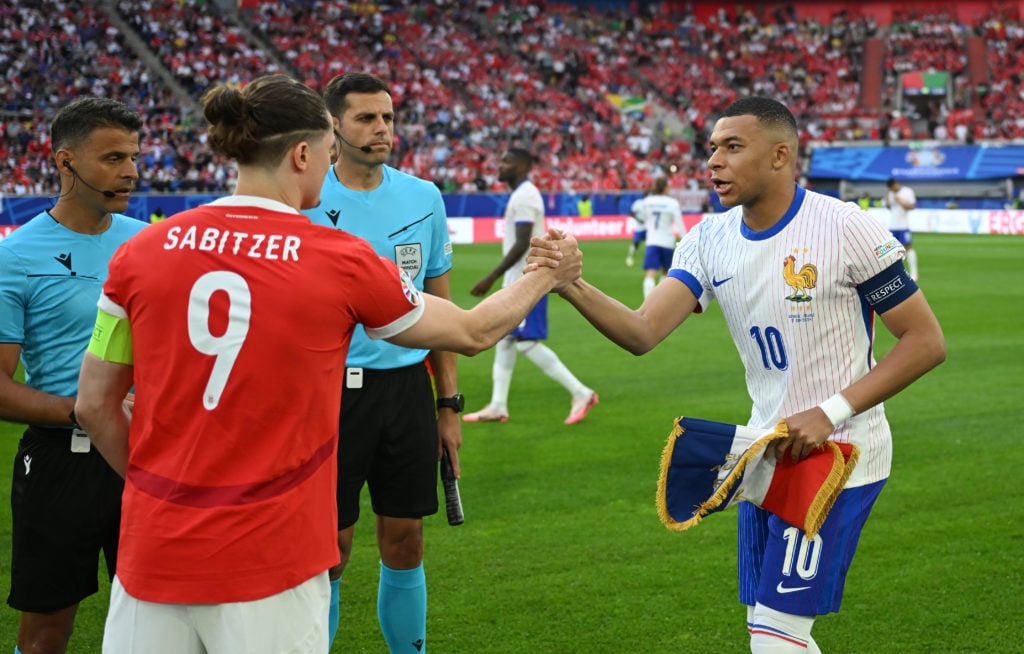 Marcel Sabitzer of Austria shakes hands with Kylian Mbappe of France as they exchange pennants prior to the EURO 2024 group stage match between Aus...