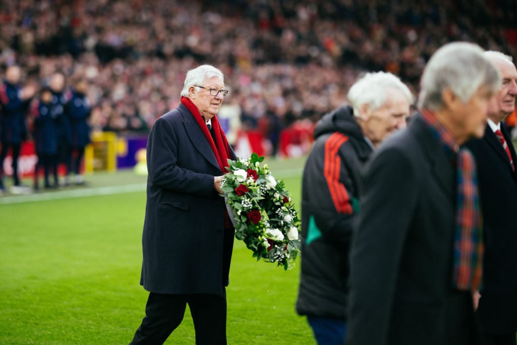 Sir Alex Ferguson carries a wreath of flowers during a tribute for late Manchester United player Denis Law prior to the Premier League match betwee...