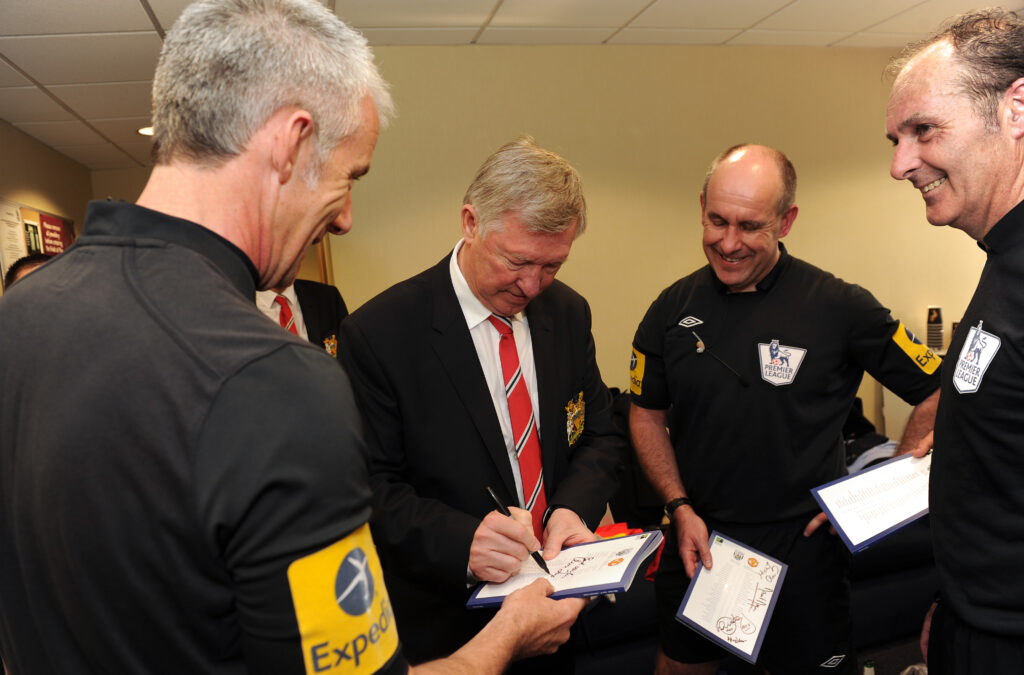 Sir Alex Ferguson signing autographs in 2013 for officials